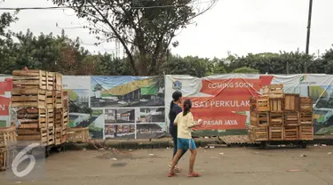 Warga berjalan diantara peti buah di samping lokasi pembangunan pusat perkulakan, Pasar Induk, Kramat Jati, Jakarta, Senin (16/1). Pemerintah Provinsi (Pemprov) DKI Jakarta berencana membangun pusat perkulakan di Kramat Jati. (Liputan6.com/Yoppy Renato)