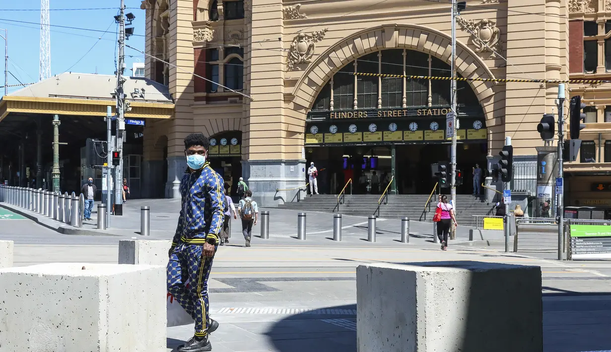 Seorang pria dengan masker berjalan melewati Stasiun Flinders Street di Melbourne, Australia, Rabu (28/10/2020). Melbourne, kota terbesar kedua Australia, akhirnya dibuka kembali usai pemberlakuan lockdown yang ketat selama lebih dari tiga bulan akibat Covid-19.  (AP Photo/Asanka Brendon Ratnayake)