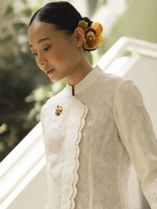 Rambutnya ditata sanggul bawah dengan hiasan bunga anggrek kuning besar. Bagian depan tertata rapi belah dua. [@brandonsalim]