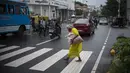 Seorang wanita tua yang mengenakan masker berjalan tanpa alas kaki melalui zebra cross di Kochi, negara bagian Kerala, India, Rabu (6/7/2022). Negara bagian selatan itu telah mewajibkan penggunaan masker di tempat-tempat umum menyusul meningkatnya kasus COVID-19. (AP Photo/ RS Iyer)