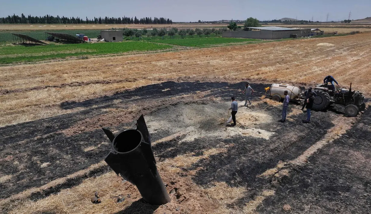 Para petani menyemprotkan air di ladang pertanian yang terbakar di dekat proyektil rudal yang jatuh di dekat kota Najha, Suriah, Senin 8 Juni 2026. (AP Photo/Ghaith Alsayed)