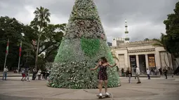 Seorang skaterboarder melewati depan pohon Natal yang terbuat dari botol plastik daur ulang di Caracas, Venezuela, Selasa (13/12/2022). Pohon Natal setinggi 10 meter tersebut merupakan proyek yang didukung kantor wali kota Caracas dan masyarakat umum yang berkontribusi dengan mengumpulkan botol dari jalanan. (Yuri CORTEZ / AFP)