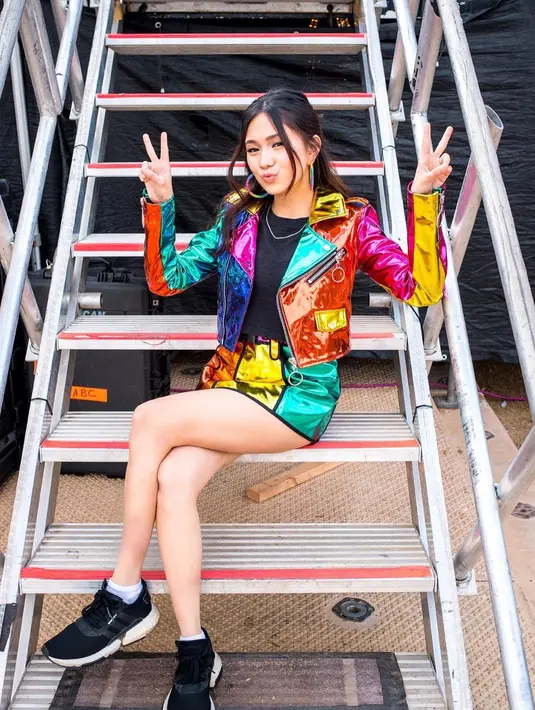 Berpose di tangga panggung, Niki terlihat colorful mengenakan set jaket dan mini skirt berwarna-warni pelangi. Ia juga tampak mengenakan crop top hitam sebagai innerwear. Foto: Instagram.