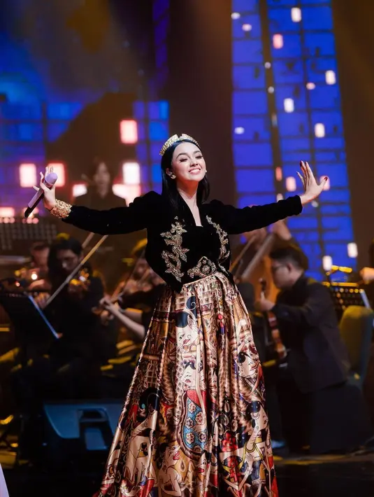 Penampilan luar biasa kali ini dipersembahkan ketika Lyodra mengenakan busana khas putri raja. Dengan atasan seperti beskap hitam dari bahan beludru hitam yang melapisi innerwear hitam, Lyodra menyempurnakan penampilannya dengan rok panjang bercorak batik. Detail seperti payet di bagian blazer dan beltnya, serta headpiece emas yang dikenakannya menambah kental kesan princess. Foto: Instagram.