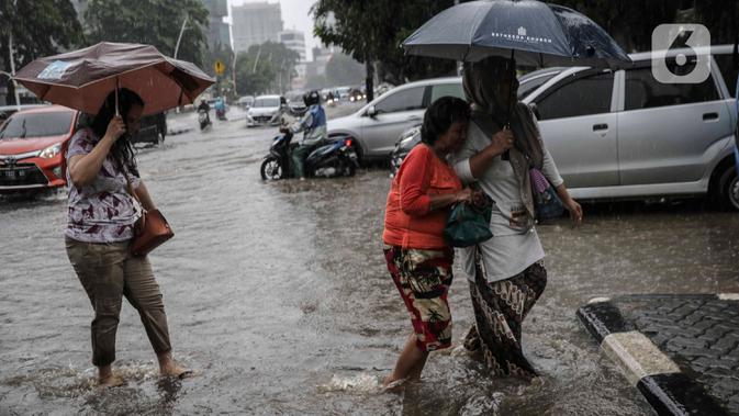 Pejalan kaki melintasi genangan air di Jalan Medan Merdeka Timur, Jakarta, Jumat (24/1/2020). Hujan deras yang mengguyur Jakarta sejak pagi tadi mengakibatkan genangan air di Jalan Medan Merdeka Timur. (Liputan6.com/Faizal Fanani)
