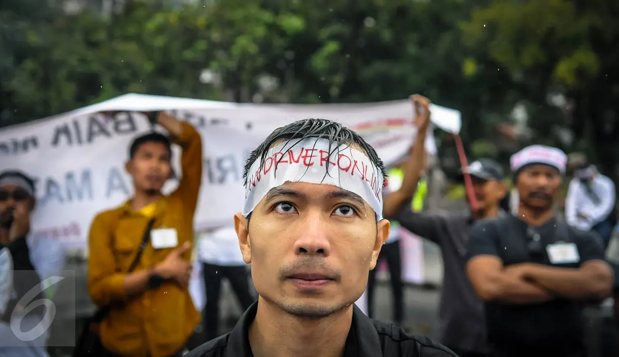 Seorang massa dari Asosiasi Driver Online (ADO) mengenakan ikat kepala di depan Istana, Jakarta, Senin (19/9). Mereka menolak diberlakukannya ujian kendaraan bermotor (KIR) menggunakan SIM A UMUM per 1 Oktober 2016. (Liputan6.com/Faizal Fanani)