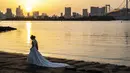 Sepasang kekasih berpose selama pemotretan pernikahan pada hari yang cerah di tepi teluk di daerah Odaiba Tokyo (12/4/2022). Para pengunjung biasanya datang ke Seaside Park untuk menikmati pemandangan Gunung Fuji dari bianglala Daikanransha. (AFP/Charly Triballeau)