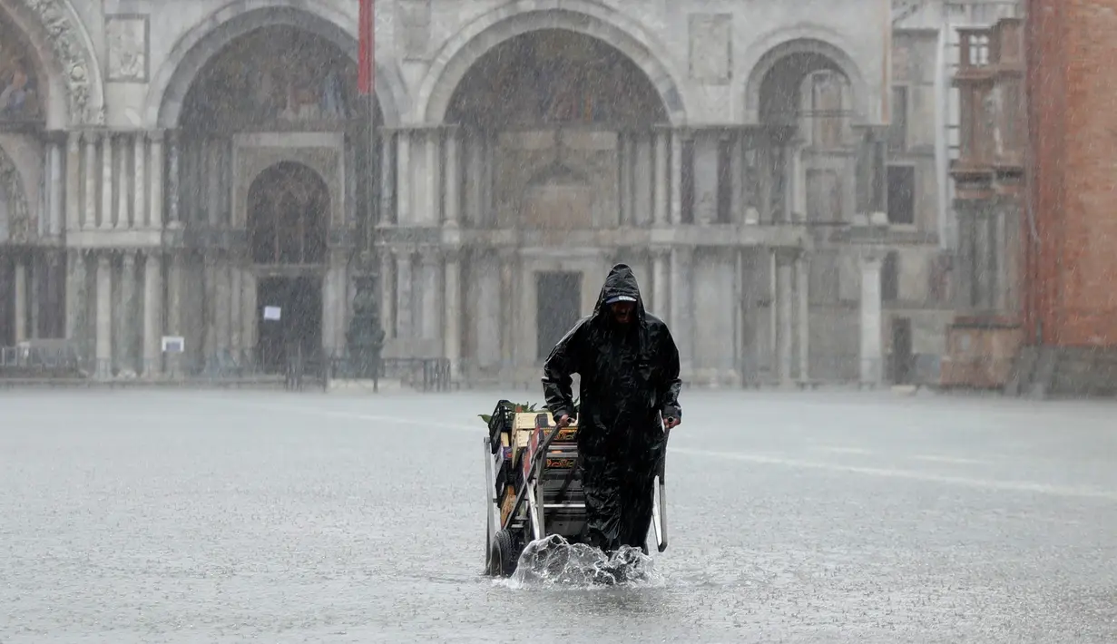 Penjual sayur membawa gerobaknya ketika gelombang pasang membuat banjir Lapangan Santo Markus di Venesia, Italia, Selasa (12/11/2019). Venesia dilanda banjir akibat gelombang pasang setinggi 127 cm. (AP Photo/Luca Bruno)