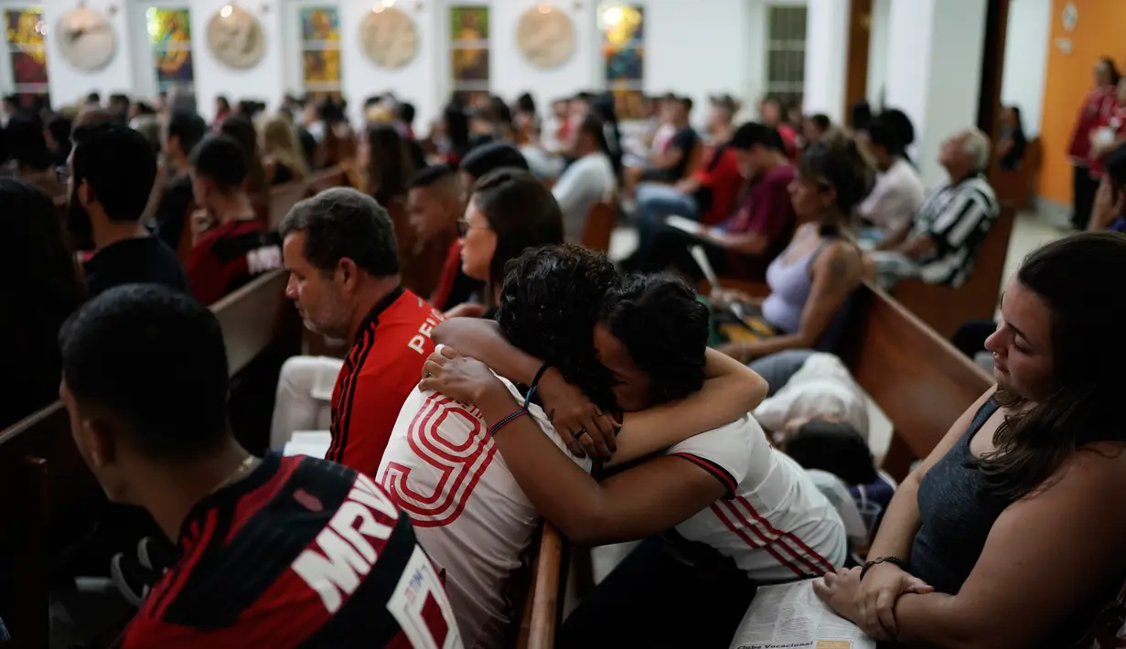Dua wanita mengenakan jersey Flamengo berpelukan saat Misa peringatan untuk para korban kebakaran di akademi sepakbola Brasil, di Rio de Janeiro, Brasil (8/2). Kebakaran merajalela ketika para peman sedang tertidur pulas. (AP Photo/Leo Correa)