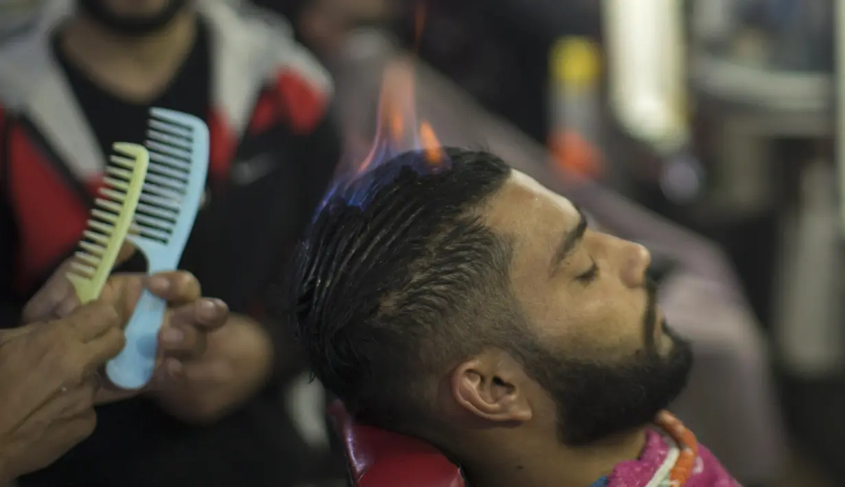 Pelanggan memotong rambutnya di barbershop milik Ramadan Edwan, seorang tukang cukur asal Palestina, di kamp pengungsian Rafah, di selatan Jalur Gaza, Rabu (1/2). Ramadan Edwan menggunakan api untuk mencukur rambut pelanggannya(MAHMUD HAMS/AFP)