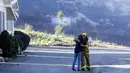 Pemadam kebakaran Simon Garcia, dari Heartland Fire Dept, mendapat pelukan dari seorang wanita setelah dia tiba untuk menemukan rumahnya masih utuh di Rancho Monserate Country Club di Fallbrook, California (8/12). (AP Photo / Gregory Bull)
