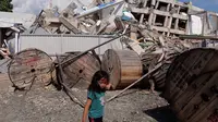 Seorang anak berjalan melewati sebuah gedung yang runtuh setelah gempa dan tsunami di Palu, Selasa (2/10). Data terbaru BNPB menunjukkan, korban tewas akibat tsunami dan gempa di Sulawesi Tengah sudah mencapai 1.347 orang. (AFP/YUSUF WAHIL)