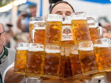 Oliver Struempfel membawa gelas bir sebanyak-banyaknya sambil berjalan untuk memecahkan rekor saat bersaing pada festival tradisional Gillamoos di Abensberg, Jerman, Minggu (3/9). Struempfel berhasil menyusun 29 gelas bir besar. (Matthias Balk/dpa via AP)