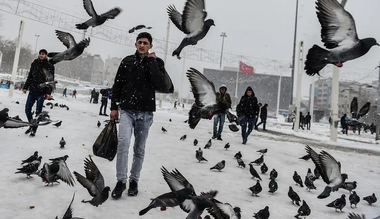 Pejalan kaki melewati kawanan burung di Taksim Square selama badai salju yang menerjang Kota Istanbul, Turki, Sabtu (7/1). Badai salju menyebabkan timbunan salju hingga setinggi 40 centimeter di sebagian wilayah kota itu. (YASIN AKGUL/AFP)