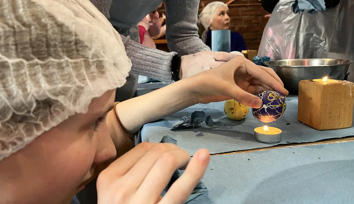 Wanita dan anak-anak Ukraina menghias telur Paskah untuk tentara dalam restoran Georgia di Lviv, Ukraina, 20 April 2022. Lebih dari selusin wanita dan anak-anak menghias telur rebus dan es roti Paskah tradisional dengan warna kuning dan biru, warna bendera Ukraina. (Alice HACKMAN/AFP)