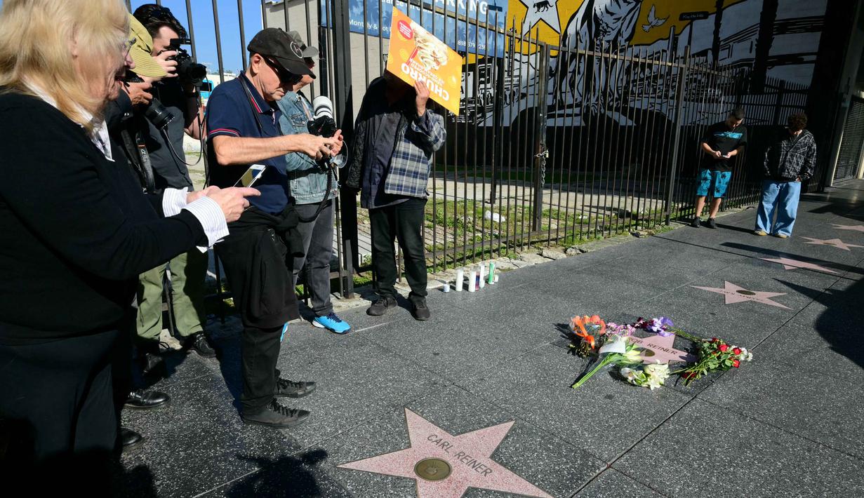 Beberapa bunga sebagai tanda belasungkawa dan penghormatan diletakkan di bintang Hollywood Walk of Fame milik aktor sekaligus sutradara Amerika Serikat, Rob Reiner, di Los Angeles, California. Tampak dalam foto, orang-orang mengambil foto bintang Hollywood Walk of Fame milik aktor sekaligus sutradara Amerika Serikat, Rob Reiner dan ayahnya, Carl Reiner, di Los Angeles, California, pada Senin 15 Desember 2025. (Frederic J. Brown/AFP)