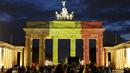 Sejumlah orang berdiri di depan gerbang Brandenburg di Berlin, Jerman, yang berubah warna menjadi bendera Belgia, Selasa (22/3). Hal itu sebagai bentuk penghormatan terhadap korban serangan bom Brussels. (REUTERS/Fabrizio Bensch)