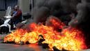 Seorang pria mengendarai skuternya melewati ban yang terbakar di salah satu jalan utama selama protes terhadap kenaikan harga barang-barang konsumsi dan jatuhnya mata uang lokal di Beirut, Lebanon, Senin (29/11/2021). (AP Photo/Hussein Malla)