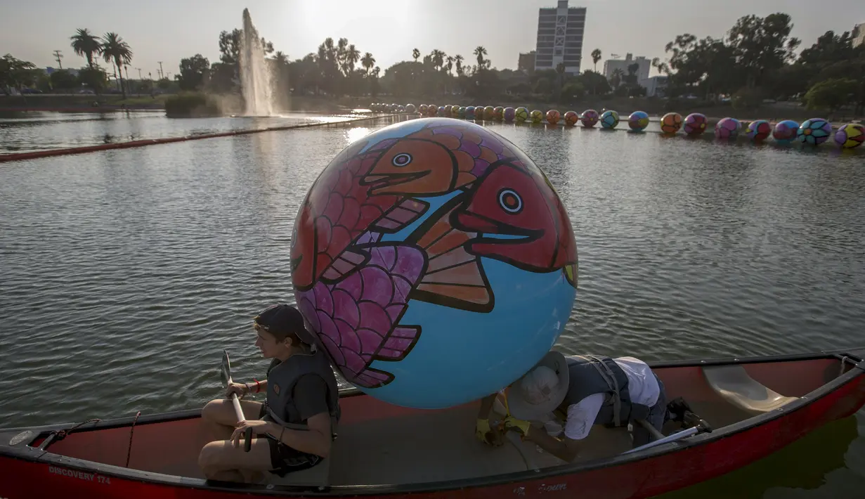 Relawan mengunakan perahu bersiap menurunkan bola raksasa ke danau MacArthur Park selama pameran "Spheres" di Los Angeles, California, AS (21/8/2015). Acara ini menampilkan sekitar 3.000 bola raksasa yang dihias oleh para relawan. (REUTERS/Mario Anzuoni)
