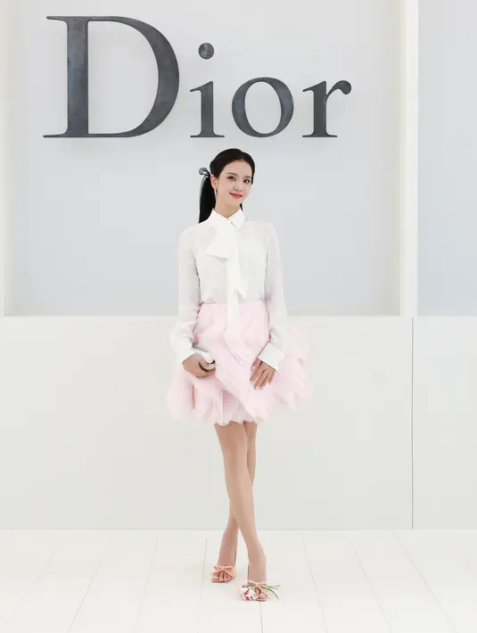 Jisoo tampil manis dengan blus putih berpita di leher dan rok tulle ruffle pink menggelembung. Clutch berbentuk angsa dan heels pita peach berhias bunga. [dok. Dior]