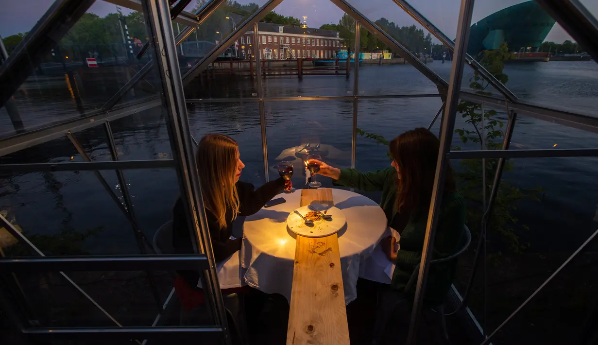Pengunjung duduk bersulang dalam kabin kaca berkonsep  "quarantine greenhouses" selama uji coba, ketika Belanda berjuang melawan penyebaran COVID-19, di restoran Mediamatic, Amsterdam pada 5 Mei 2020. (AP/Peter Dejong)