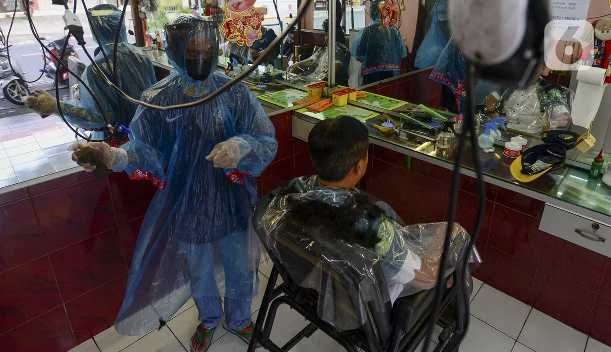 Tukang cukur mengenakan alat pelindung diri (APD) dari plastik saat mencukur rambut pelanggan di Pondok Kelapa, Jakarta, Selasa (5/5/2020). Tukang cukur mengenakan APD untuk mengurangi risiko penularan virus corona COVID-19. (merdeka.com/Imam Buhori)