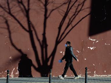 Seorang warga yang mengenakan masker berjalan dekat bayang-bayang pohon di Beijing, China, 27 Desember 2022. Perusahaan menyambut baik keputusan China untuk mengakhiri karantina bagi pelancong dari luar negeri sebagai langkah penting untuk menghidupkan kembali aktivitas bisnis yang merosot, sementara Jepang mengumumkan pembatasan pengunjung saat infeksi melonjak. (AP Photo/Ng Han Guan)