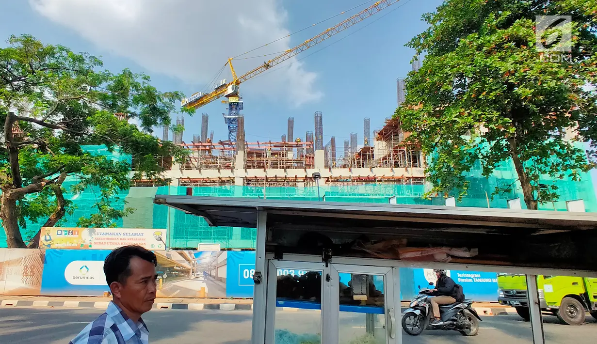 Pejalan kaki berjalan di depan pembangunan rumah susun terintegrasi dengan sarana transportasi di samping Stasiun KA Tanjung Barat, Jakarta Selatan, Kamis (11/7.2019). Pembangunan hunian TOD Tanjung Barat merupakan hasil kerja sama PT KAI dan Perum Perumnas. (Liputan 6.com/Immanuel Antonius)