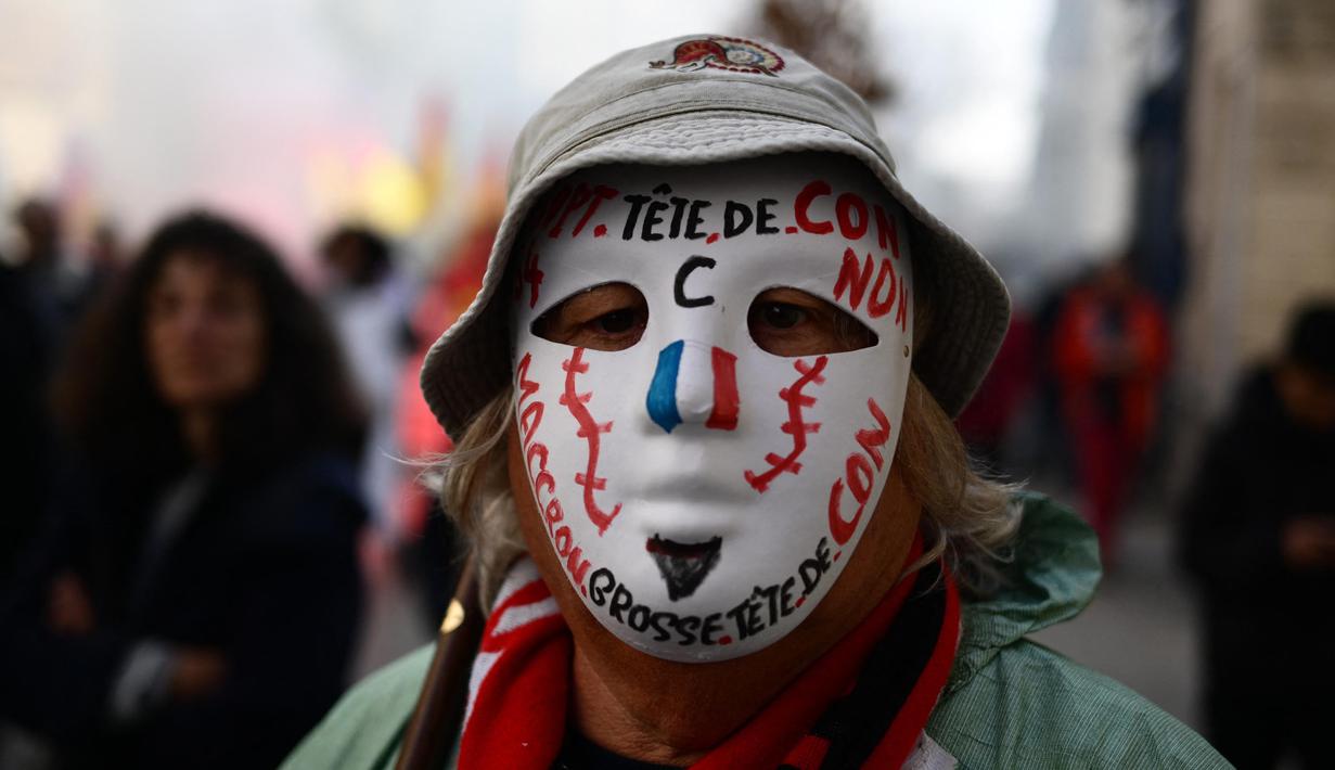 Seorang pengunjuk rasa mengenakan topeng bertuliskan slogan-slogan selama demonstrasi pada hari kelima demonstrasi nasional yang diselenggarakan sejak awal tahun, menentang perombakan pensiun yang sangat tidak populer, di Avignon, Prancis Selatan, Kamis (16/2/2023). (CHRISTOPHE SIMON/AFP)