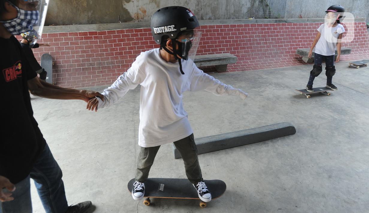 Instruktur melatih seorang anak menggunakan skateboard dengan memakai masker dan face shield di Crooz Shophouse di kawasan Duren Tiga, Jakarta Selatan, Minggu (2/8/2020). Mereka kembali melakukan latihan seminggu dua kali dengan menerapkan protokol kesehatan. (merdeka.com/Arie Basuki)
