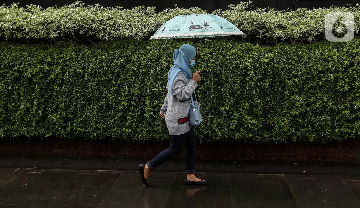 Seorang warga menggunakan payung saat hujan di kawasan Jakarta, Selasa (16/2/2021). Sebagai tahap awal vaksinasi COVID-19 tahap kedua bagi pekerja publik akan dimulai dari para pedagang Pasar Tanah Abang pada Rabu 17 Februari 2021. (Liputan6.com/Johan Tallo)