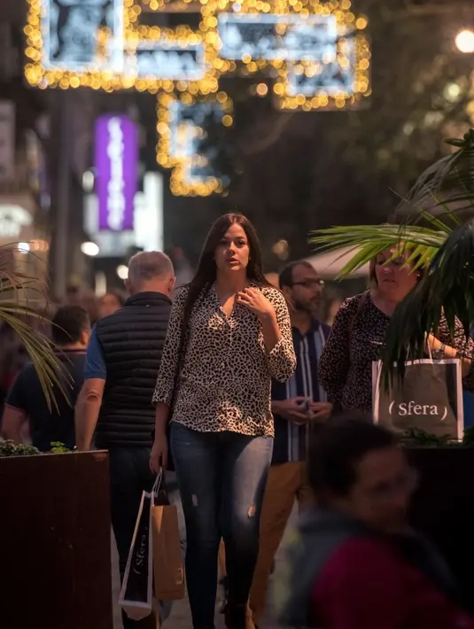 Seorang wanita berjalan di bawah lampu Natal yang menghiasi jalan Santa Cruz de Tenerife di pulau Canary Tenerife, Spanyol (19/12). (AFP Photo/Desiree Martin)