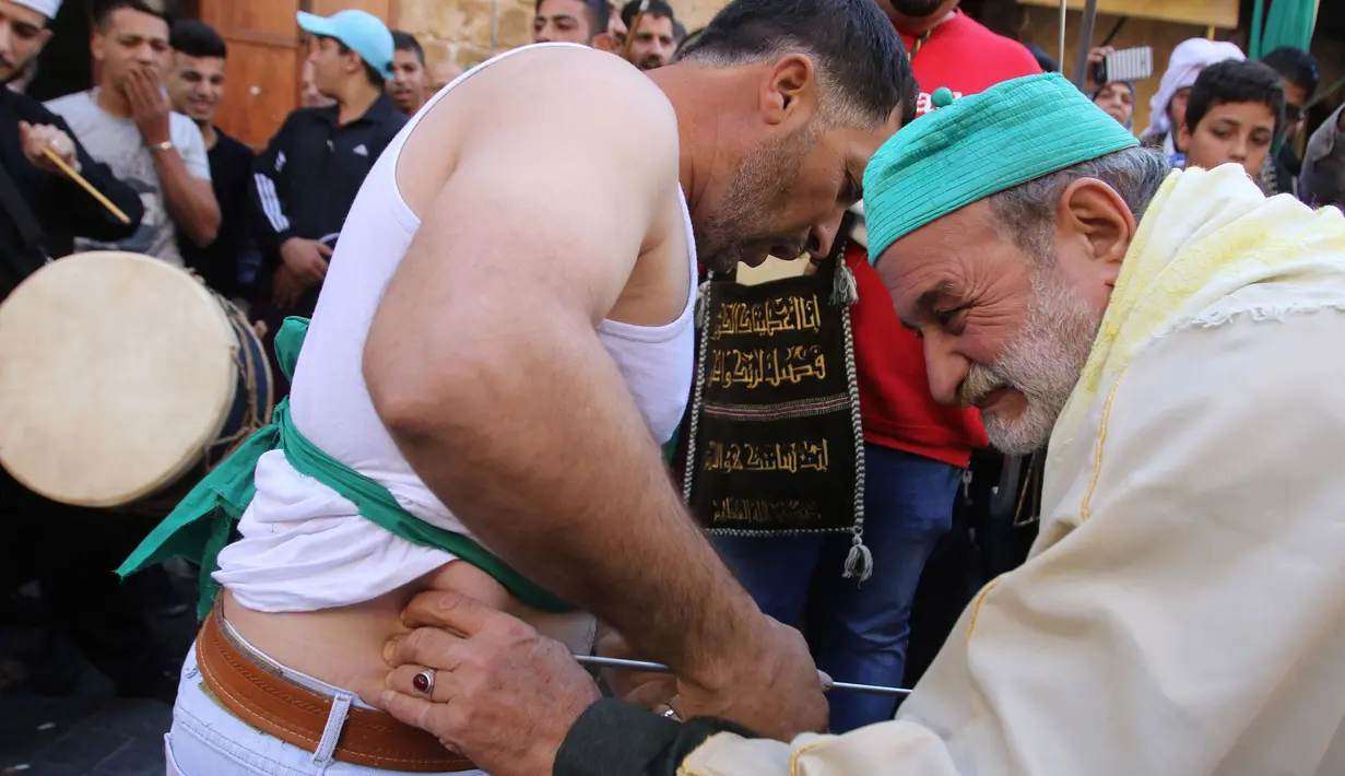 Warga muslim Sufi menusukkan benda tajam ke perut salah satu peserta saat perayaan Maulid Nabi Muhammad SAW di Sidon, Lebanon (30/11). Tradisi yang mirip debus ini selalu digelar setiap tahunnya. (AFP Photo/Mahmoud Zayyat)