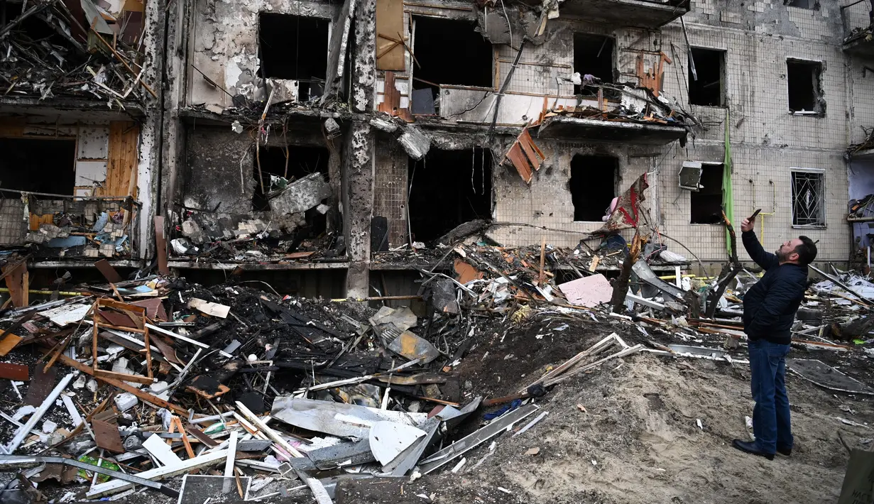 Seorang pria mengambil gambar sebuah bangunan tempat tinggal yang rusak setelah peluru militer Rusia menghantam di Koshytsa Street, Kiev, Ukraina (25/2/2022). Pasukan Rusia mencapai pinggiran Keiv pada hari Jumat (24/2). (AFP/Daniel Leal)
