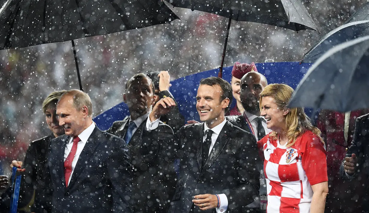 Presiden Rusia Vladimir Putin (kiri) bersama Presiden Prancis Emmanuel Macron (tengah) dan Presiden Kroasia Kolinda Grabar-Kitarovic berjalan dalam hujan usai laga final Piala Dunia 2018 di Stadion Luzhnik, Moskow, Rusia, Minggu (15/7). (Franck Fife/AFP)