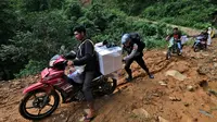 Seorang petugas polisi membantu petugas pemilu mendorong sepeda motor mendaki bukit saat mendistribusikan kotak suara dan perlengkapan pemilu lainnya ke tempat pemungutan suara (TPS) di desa-desa terpencil di Maros, Sulawesi Selatan, Selasa, 13 Februari 2024. (AP Photo/Masyudi S. Firmansyah)