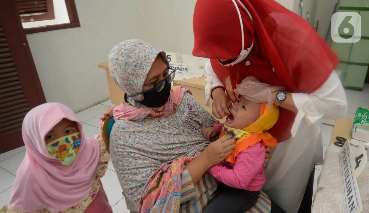 Bidan dibantu Kader Posyandu memberikan vaksin vitamin A dan imunisasi di Posyandu RW 20, Kelurahan Pondok Benda, Tangerang Selatan, Selasa (18/8/2020). Pemerintah sudah mengaktifkan pelayanan posyandu ketiga sejak pandemi Covid-19 dengan memperketat protokol kesehatan. (merdeka.com/Dwi Narwoko)