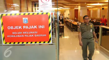 Petugas berjalan di samping stiker penunggak pajak yang dipasang di sebuah restoran di pusat perbelanjaan di kawasan Senayan, Jakarta, Senin (5/9). Pemasangan stiker dilakukan Dinas Pelayanan Pajak DKI lantaran menunggak pajak. (Liputan6.com/Angga Yuniar)