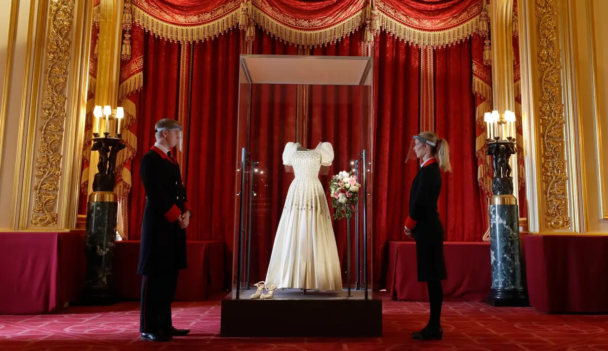 Petugas kerajaan berdiri di samping gaun pengantin Putri Beatrice yang dipajang di Kastil Windsor, Windsor, Rabu (23/9/2020). Beatrice menikah dalam balutan gaun pengantin dari era tahun 1960-an rancangan Norman Hartnell yang dipinjamkan sang nenek, Ratu Elizabeth II. (AP Photo/Kirsty Wigglesworth)