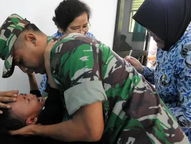 Seorang anggota TNI menenangkan anaknya yang diberi vaksin di Kantor Kesehatan Kopassus, Jakarta, Senin (18/7). Kopassus menggelar pelaksanaan vaksinasi ulang terhadap anak prajurit yang terindikasi menjadi korban vaksin palsu. (Liputan6.com/Helmi Afandi)