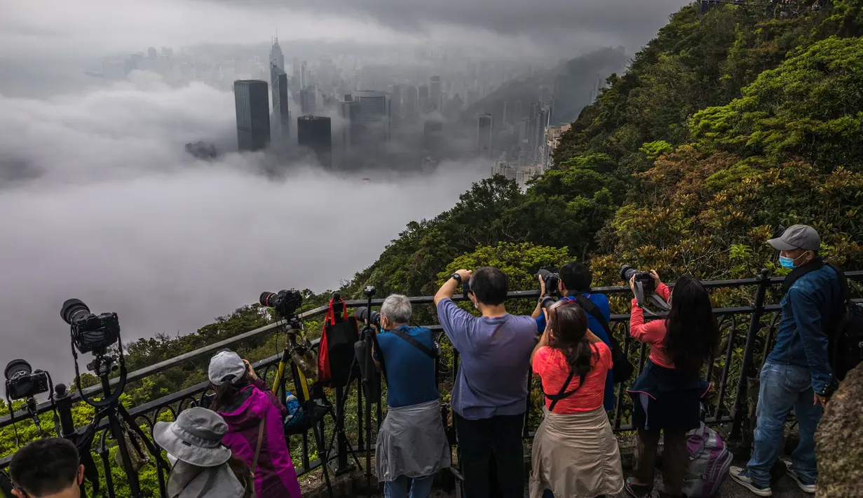Orang-orang mengambil foto kabut di atas Hong Kong, Selasa (22/3/2022). Kabut tebal menyelimuti Hong Kong pada musim semi ketika wilayah tersebut dipengaruhi oleh udara dingin dan hangat bergantian. (AFP/Dale De La Rey)