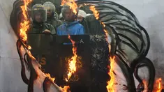 Sebuah spanduk dibakar dengan latar belakang polisi anti huru hara saat demonstrasi yang diadakan pada ulang tahun Ferdinand Marcos ke-100 di Manila (11/9). Perayaan seabad Ferdinand Marcos ini dijaga ketat petugas keamanan setempat.(AFP Photo/Ted Aljibe)