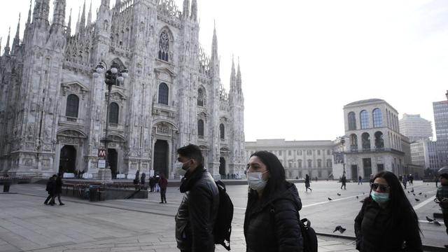 Orang-orang yang memakai masker sanitasi berjalan melewati katedral gothic Duomo di Milan, Italia, Minggu, 23 Februari 2020.