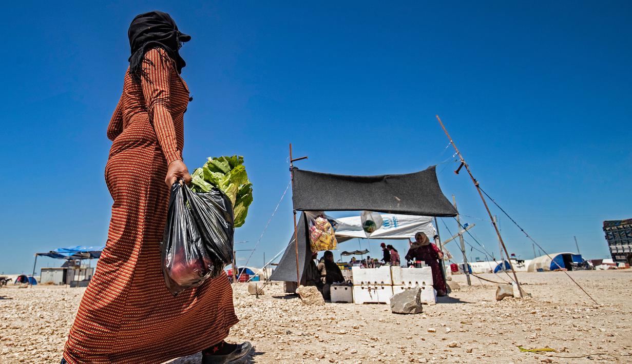 Seorang wanita Suriah yang terlantar membawa tas sayuran selama bulan suci Ramadan di kamp Washukanni untuk para pengungsi internal di provinsi Hasakeh di timur laut Suriah, (10/5/2020). (AFP/Delil Souleiman)