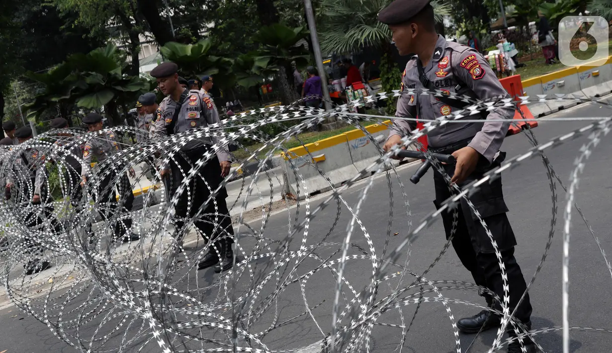Personel Kepolisian merapatkan barikade kawat berduri yang menutup ruas Jalan Medan Merdeka Barat, Jakarta, Senin (28/10/2019). Penutupan ini antisipasi aksi unjuk rasa mahasiswa mendesak Presiden Jokowi segera mengeluarkan Perppu KPK. (Liputan6.com/Helmi Fithriansyah)