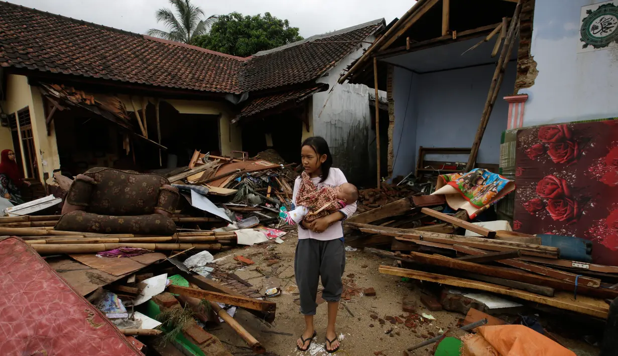 Seorang gadis menggendong bayi berjalan di dekat puing-puing di daerah yang dilanda tsunami di Carita, Banten, Kamis, (27/12). (AP Photo/Achmad Ibrahim)