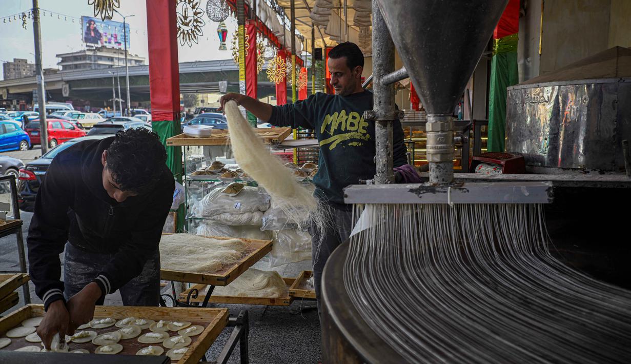 Diisi dengan kacang atau keju dan kemudian digoreng atau dipanggang, qatayef biasanya dinikmati saat berbuka puasa bersama dengan keluarga dan teman. Tampak dalam foto, para pembuat roti Mesir menyiapkan kue tradisional Qatayef (kiri) dan Kunafa (kanan), yang dibuat selama bulan suci Ramadan, di tokonya, Kairo, Mesir, pada Kamis 12 Maret 2026. (Khaled DESOUKI/AFP)