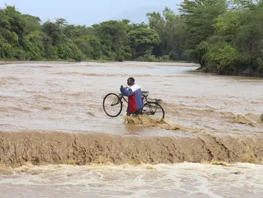 Seorang pria yang membawa sepedanya melintasi Sungai Muuoni yang banjir, dimana 8 orang dikabarkan tenggelam dalam semalam saat menyeberangi sungai di kawasan Mukaa, kabupaten Makueni, wilayah Timur Kenya, Jumat, 24 November 2023. (AP Photo)