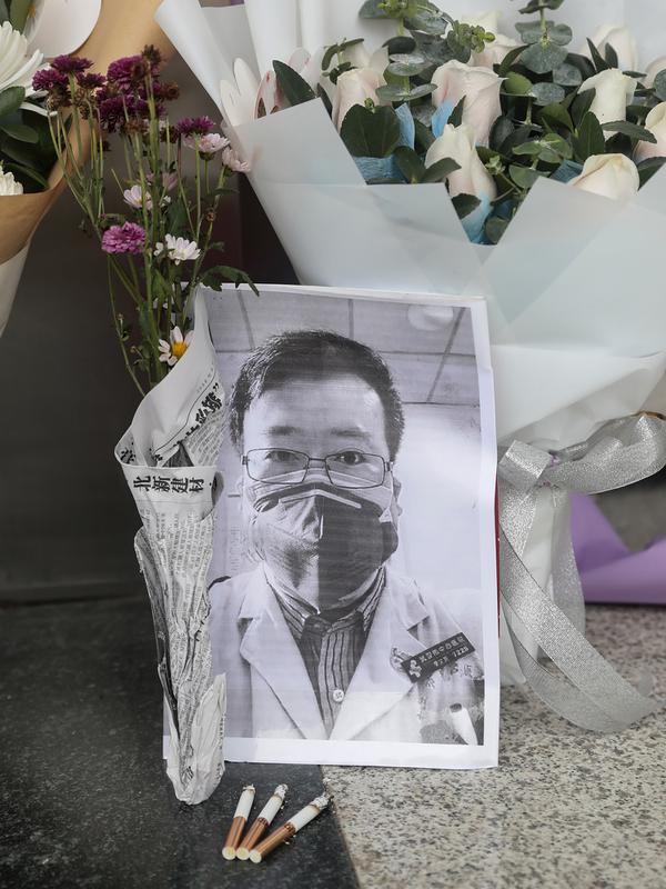 Karangan bunga dan foto mendiang dokter Li Wenliang terlihat di Cabang Houhu Rumah Sakit Pusat Wuhan di Wuhan di provinsi Hubei, China, Jumat, (7/2/2020). Li Wenliang sebelumnya memberikan peringatan kepada publik tentang potensi munculnya virus corona pada Desember 2019. (AFP/STR)