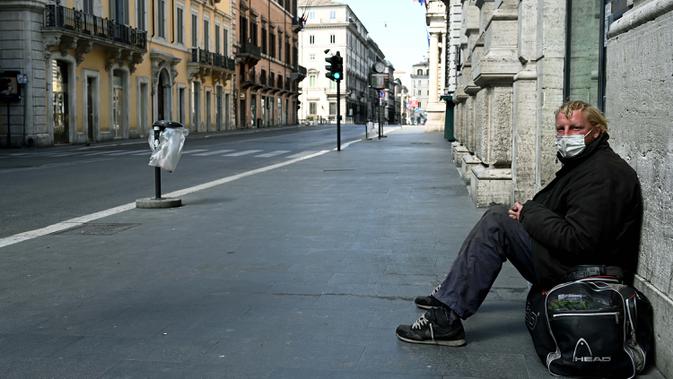 Seorang tunawisma duduk di jalan utama Via del Corso yang sepi setelah pemerintah Italia melakukan lockdown untuk menghentikan penyebaran pandemi COVID-19 di Roma pada 24 Maret 2020. (Photo by Vincenzo PINTO / AFP)